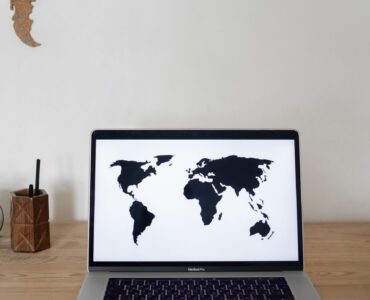 Laptop auf einem Schreibtisch mit einer Weltkarte auf dem Bildschirm und einer Weltkarte im Hintergrund.